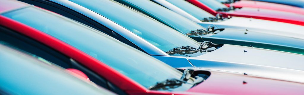 A row of parked cars in various colors lined up on a dealership lot.