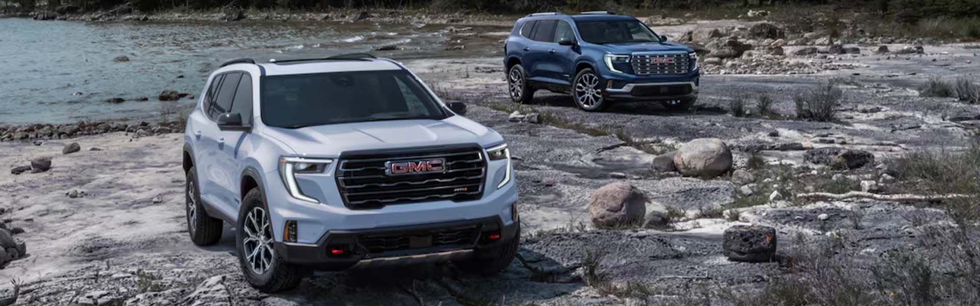 2025 GMC Acadia White and 2025 GMC Acadia Blue parked on rocks by water